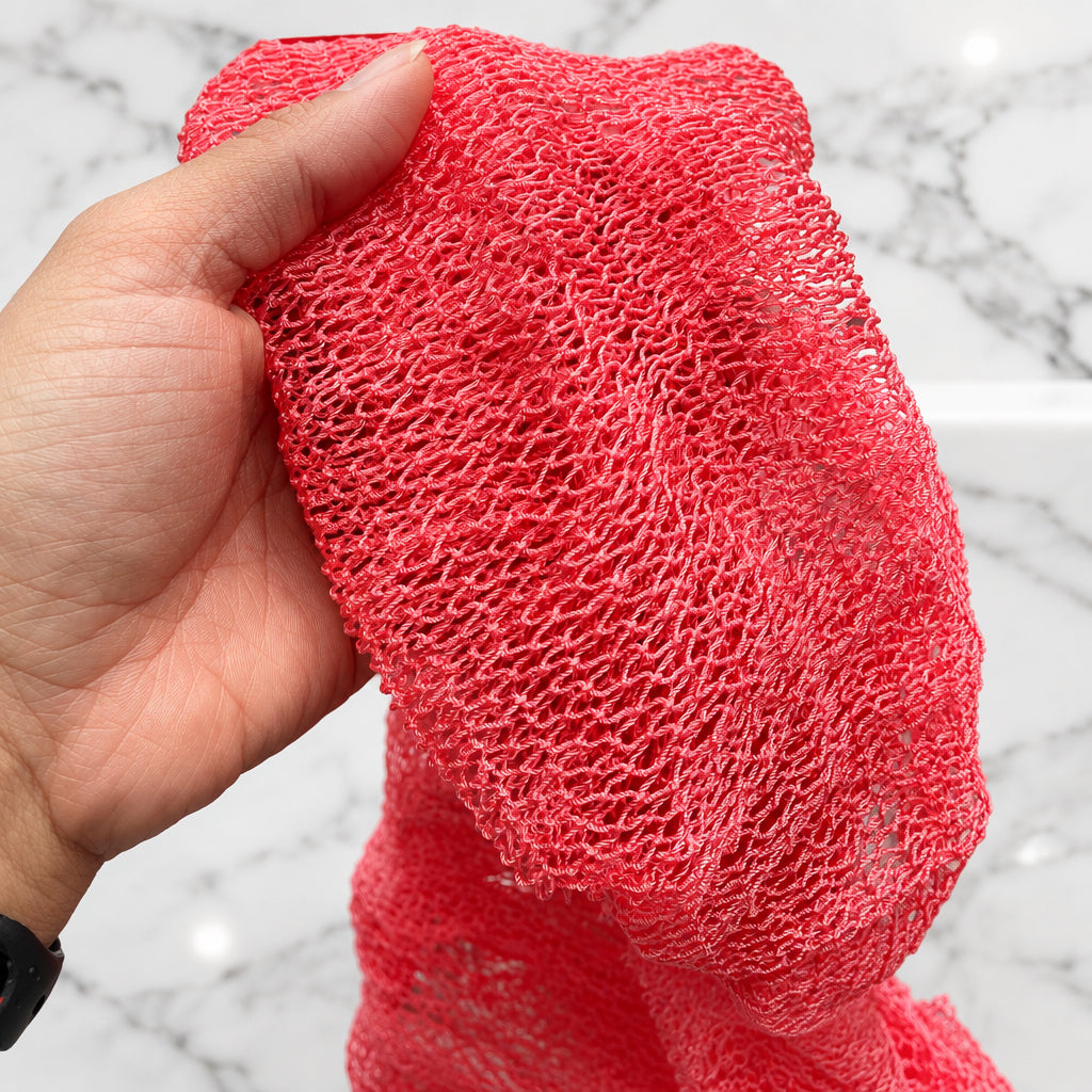 A hand holding up a coral pink mesh African Net Sponge, showing its fine woven texture and open-knit pattern.